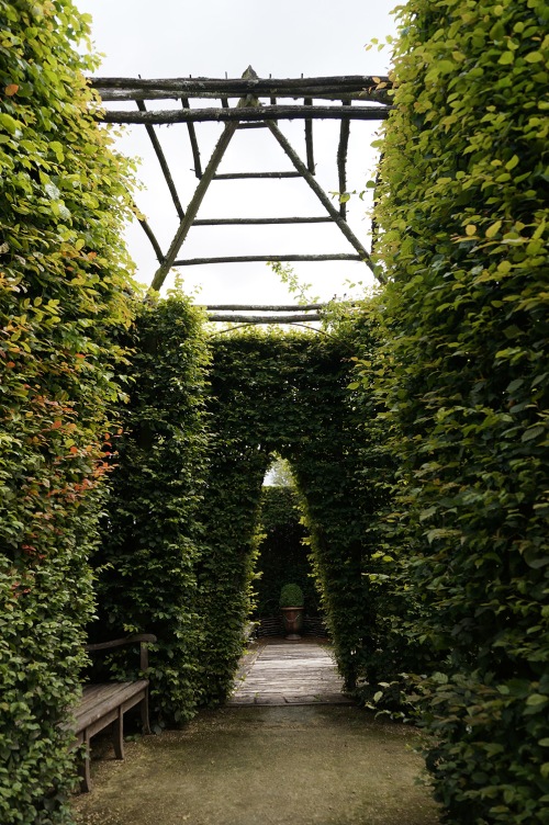A triangular doorway is carved into a hornbeam hedge and reflected in the rustic roof overhead.